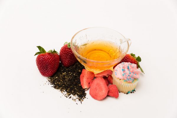 cup of strawberry cupcake tea with strawberries tea grounds and a cupcake around it